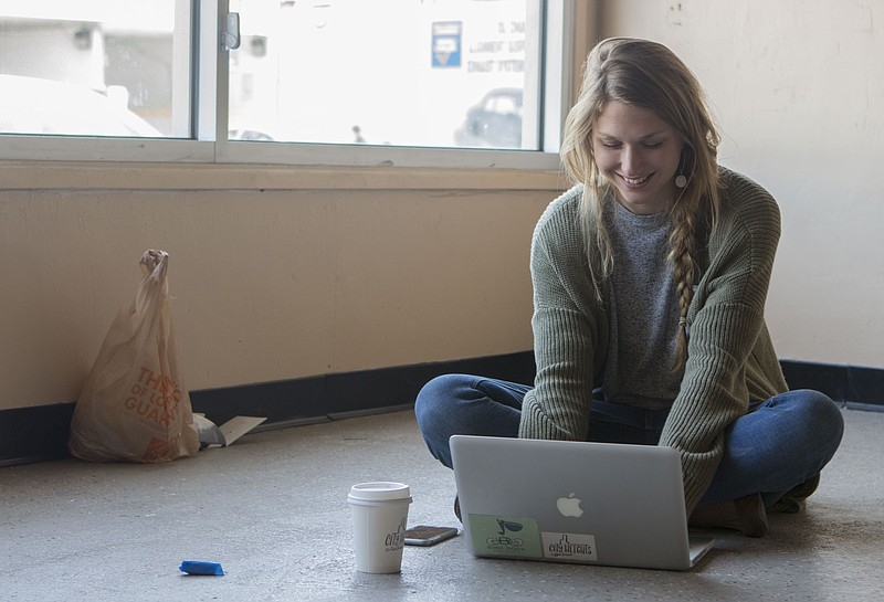 Sterling Tran sits cross-legged in front of her laptop on the floor of the future storefront location of the City Heights Coffee House